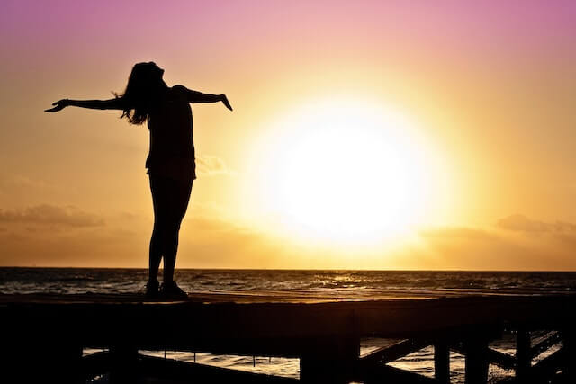 silueta de una persona con los brazos abiertos con la puesta de sol de fondo